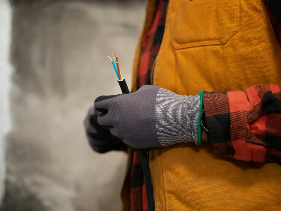 Electrician in a work vest holding a cable with stripped wires
