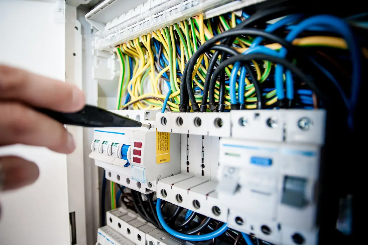 Electrician working with a screwdriver in a fuse board with coloured wires