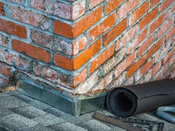 New flashing around the base of a brick chimney, with underlay and tools on the roof