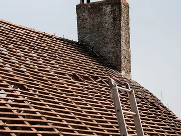 Roof being re-roofed with the old tiles taken off, with a chimney and a ladder