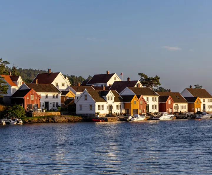 White timber houses with tiled roofs by the water in the evening sun