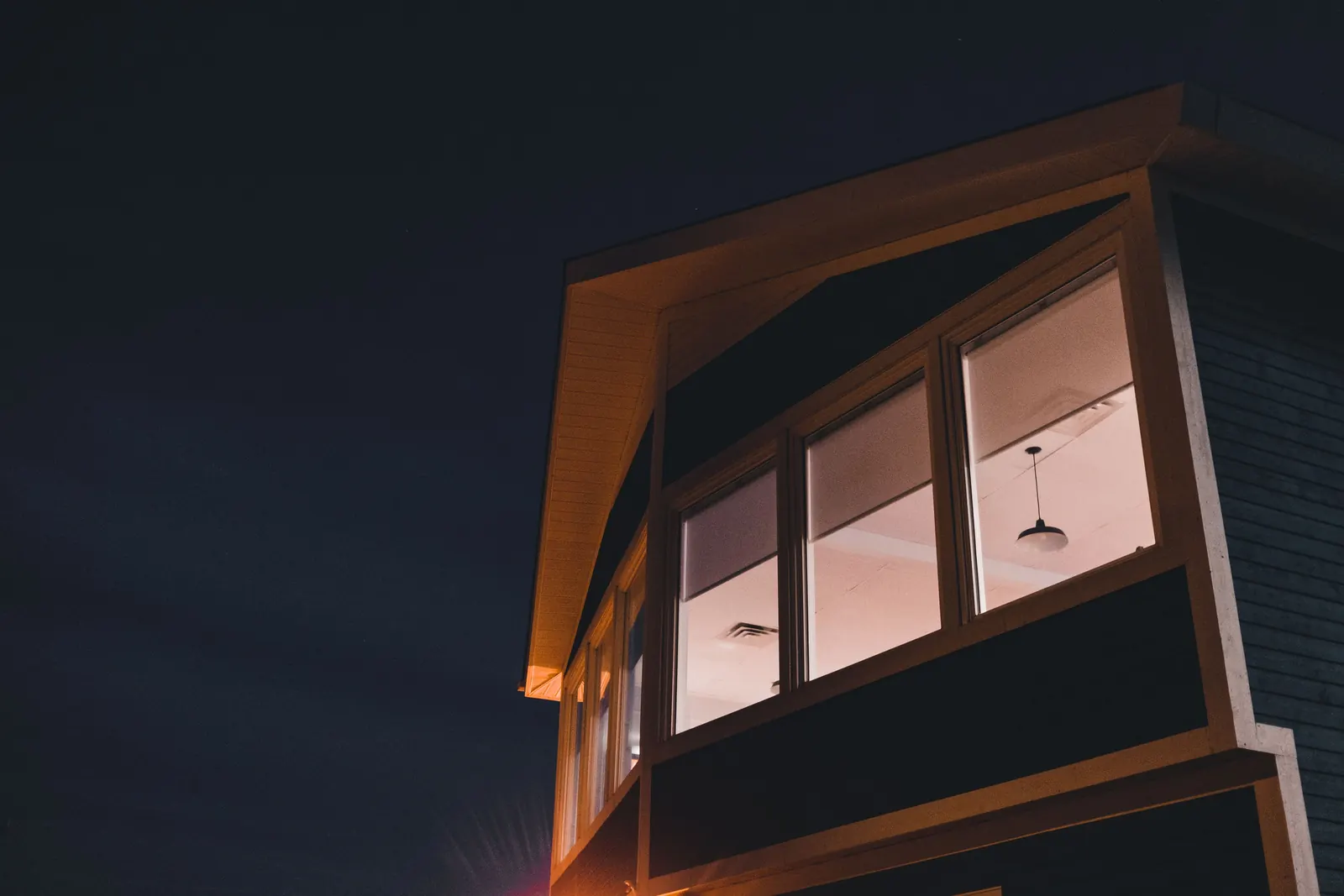 Modern house at dusk with large, warmly lit windows under the eaves