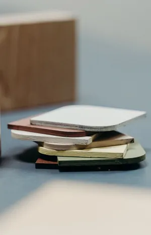 Pile of coloured material samples on a grey table, with a wooden block in the background