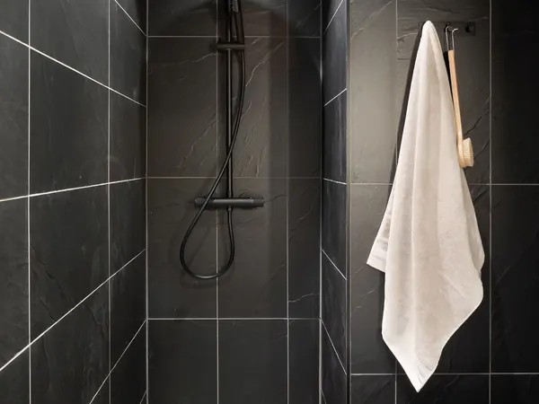Shower area with dark slate tiles, a black shower set and a white towel