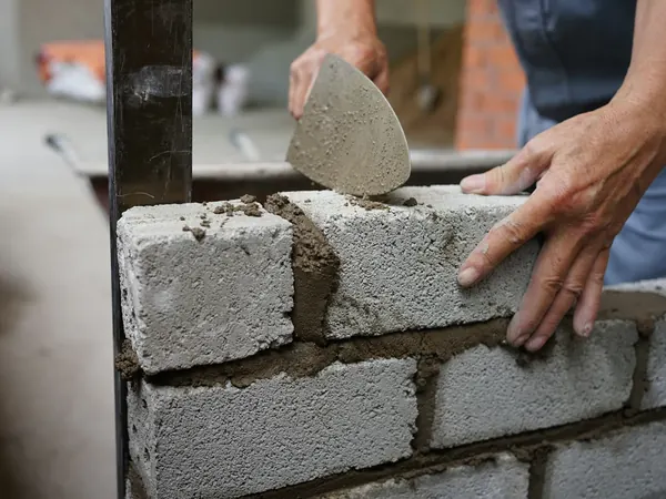 Murer legger betongblokker i mørtel med murskje